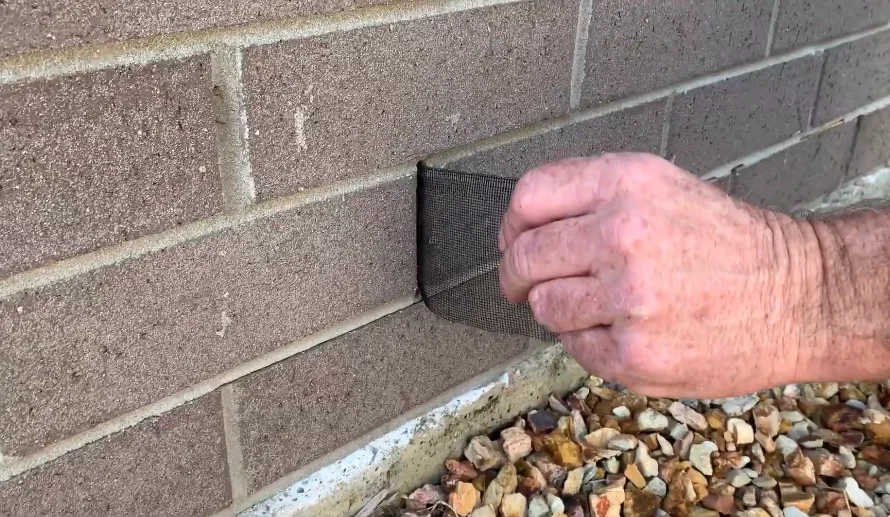 Weep hole cover being pressed into a brick wall to block mice